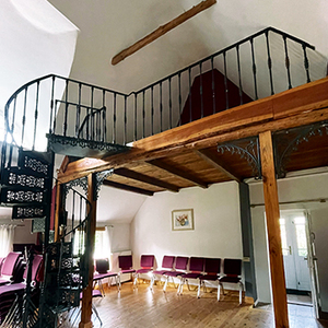 Eine schmiedeeiserne Wendeltreppe führt auf eine hölzerne Empore.